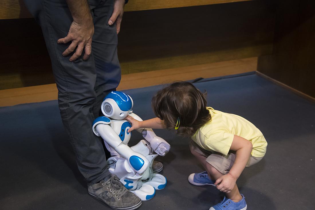 Un bambino si china per interagire con un piccolo robot umanoide NAO appoggiato sul pavimento, al Festival della Robotica.