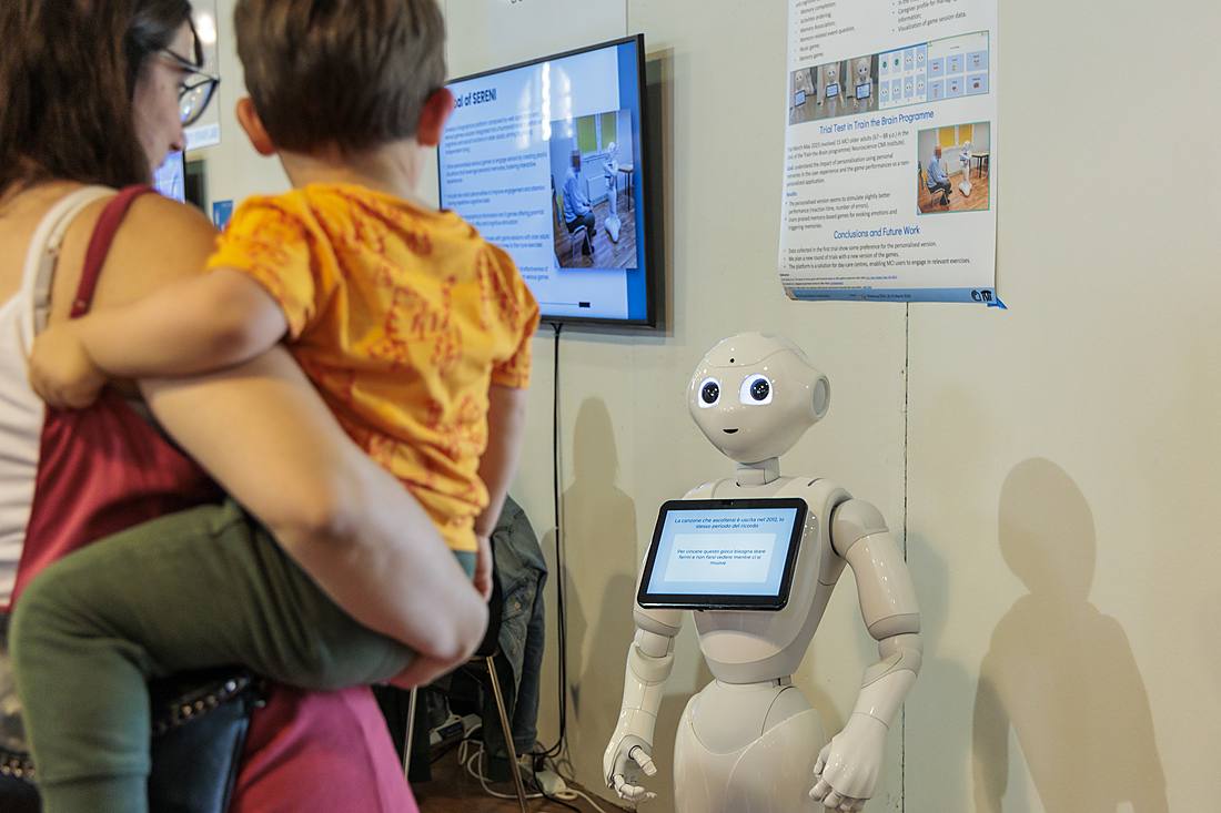 Una mamma con un bambino in braccio osserva un robot umanoide Pepper a un'esposizione del Festival della Robotica.