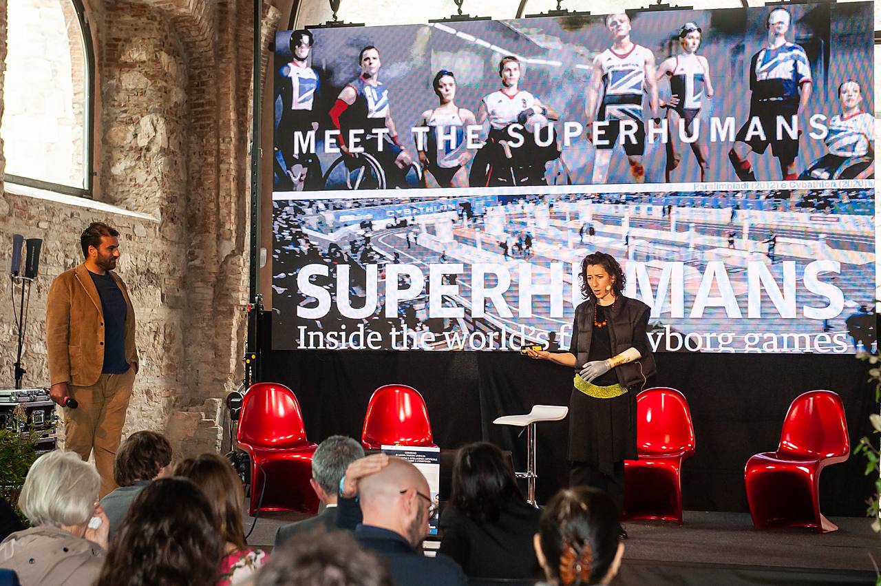 Un pubblico in sala assiste a un talk con un grande schermo che mostra la scritta «Meet the Superhumans» durante il Festival della Robotica.